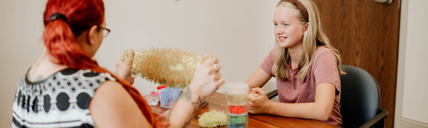 adolescent meeting with a therapist; therapist is holding up a squishy toy while adolescent looks at her