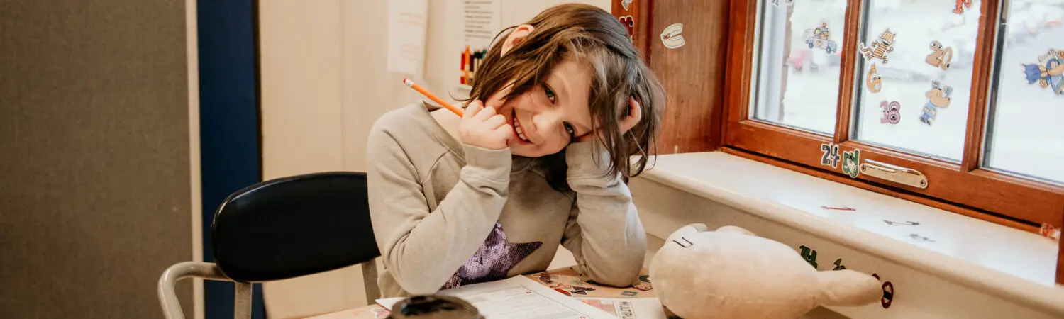 Student smiling shyly at the camera while working at her desk.