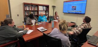 educational consultant pictured seated around a conference table with other educators sharing professional development training